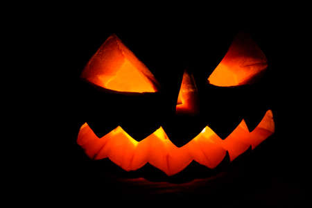 Carved halloween pumpkin jack-o-lantern glows in darknessの写真素材