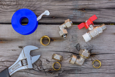 Different plumbing spare parts, sealing tape and adjustable wrench on wooden background. Top view