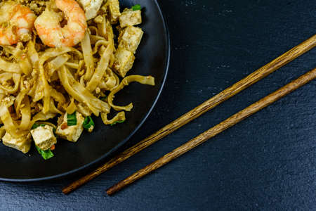 Black plate with pad thai and chopsticks on slate board. Top viewの写真素材