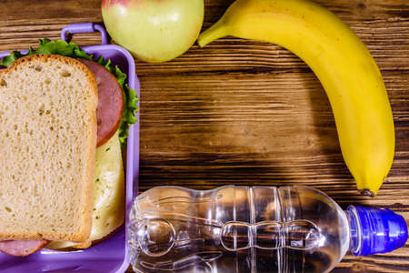 Ripe apple, banana, bottle of water and lunch box with sandwiches on wooden table. Top viewの写真素材