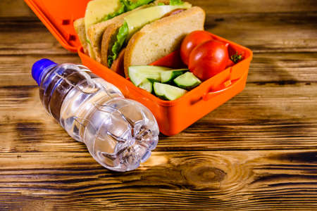 Bottle of water and lunch box with sandwiches, cucumbers and tomatoes on rustic wooden tableの写真素材