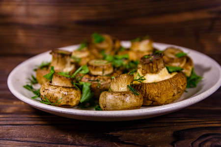 Plate with baked champignons, dill and parsley on wooden tableの写真素材