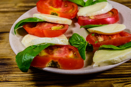 Plate with caprese salad (italian salad with cherry tomatoes, mozzarella cheese and basil leaves) on rustic wooden tableの写真素材