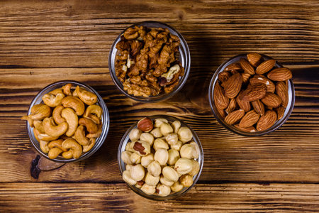 Various nuts (almond, cashew, hazelnut, walnut) in glass bowls on wooden table. Vegetarian meal. Healthy eating concept. Top viewの写真素材
