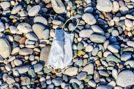 A disposable face mask discarded on pebble at beach