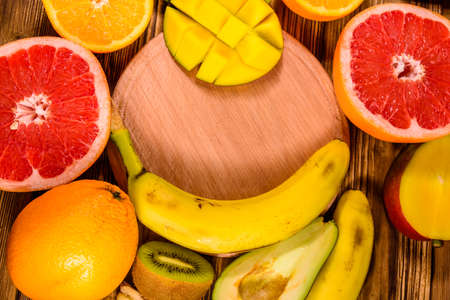 Still life with exotic fruits and cutting board. Bananas, mango, oranges, avocado, grapefruit and kiwi fruits on rustic wooden table. Top viewの写真素材