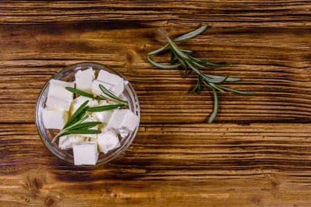 Chopped feta cheese and rosemary in glass bowl on wooden table. Top viewの写真素材