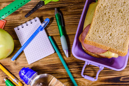 Bottle of water, ripe apple, different stationeries and lunch box with sandwiches on wooden table. Top viewの写真素材