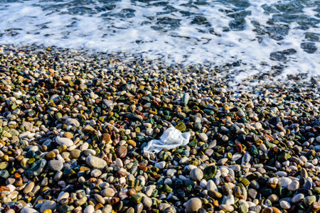 A disposable face mask discarded on pebble at beachの写真素材