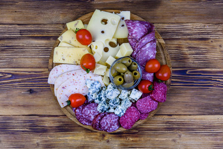 Slices of various types of cheese and dry smoked salami sausage on a wooden background. Traditional...