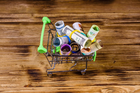 Many rolled up banknotes in small shopping cart. Euro, american dollars, ukrainian hryvnias,...