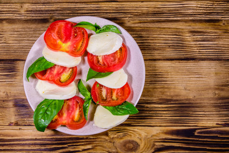 Plate with caprese salad (italian salad with cherry tomatoes, mozzarella cheese and basil leaves) on rustic wooden table. Top viewの写真素材