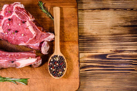 Raw ribeye steak, wooden spoon with spices and rosemary on cbtting board. Top viewの写真素材