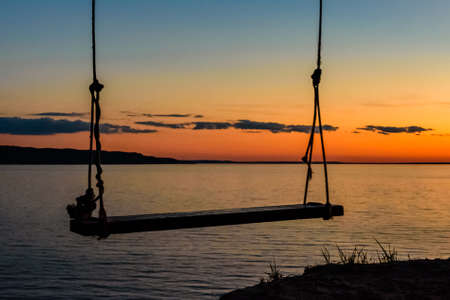 Empty swing hanging from tree at bank of river Dnieper at sunsetの写真素材