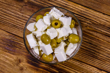 Chopped feta cheese and olives in glass bowl on wooden table. Top viewの写真素材