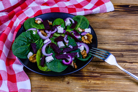Salad with spinach leaves, feta cheese, beetroot, walnuts and onion on black plate