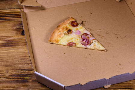 Last piece of pizza with sausages, ham and parmesan cheese in cardboard boxの写真素材