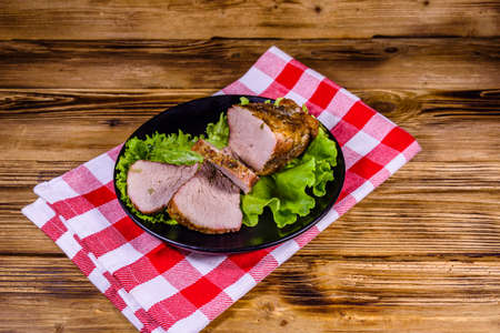 Slices of baked pork meat and lettuce leaves on black plateの写真素材