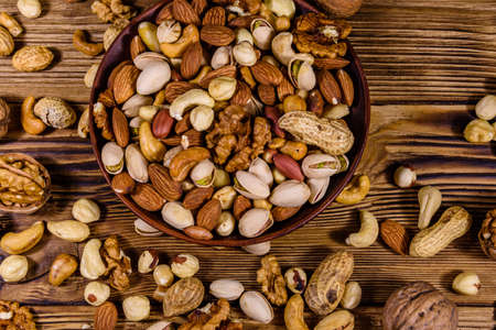 Various nuts (almond, cashew, hazelnut, pistachio, walnut) in ceramic plate on wooden table. Vegetarian meal. Healthy eating concept. Top viewの写真素材