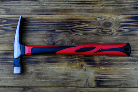 Masonry hammer with red handle on wooden background. Top view