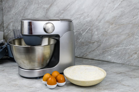 Modern food processor, eggs and plate with flour on kitchen table