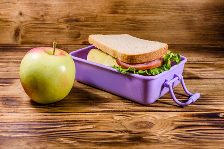 Ripe apple and lunch box with sandwiches on wooden tableの写真素材
