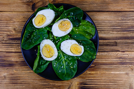 Spinach leaves and halved boiled eggs on black plate. top viewの写真素材