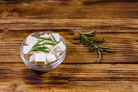 Chopped feta cheese and rosemary in glass bowl on wooden tableの写真素材