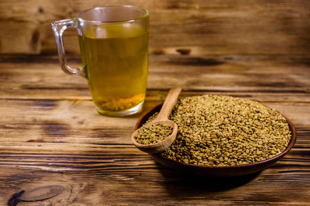 Cup of yellow tea (methi dana) and plate with fenugreek seeds on rustic wooden tableの写真素材