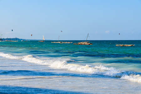 Traditional wooden fishing boat dhows at the Zanzibar island, Tanzania. Kitesurfers on background