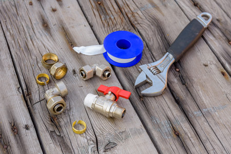 Different plumbing spare parts, sealing tape and adjustable wrench on wooden background