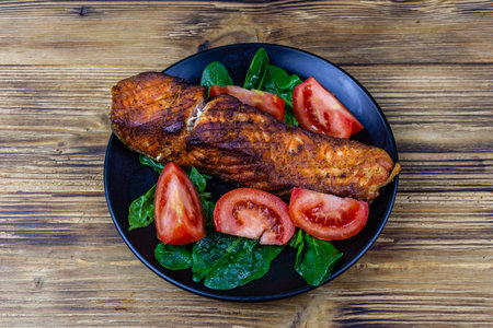 Plate with roasted salmon steak, tomatoes and spinach leaves on wooden table