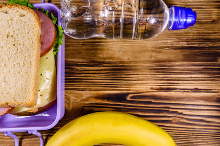 Ripe apple, banana, bottle of water and lunch box with sandwiches on wooden table. Top viewの写真素材