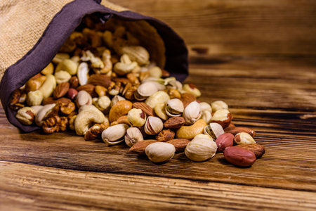 Various nuts (almond, cashew, hazelnut, pistachio, walnut) scattered from bag on wooden table. Vegetarian meal. Healthy eating conceptの写真素材