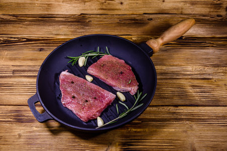 Raw steaks with garlic, rosemary and spices in cast iron grill panの写真素材