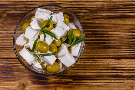 Chopped feta cheese, rosemary and olives in glass bowl on wooden table. Top viewの写真素材