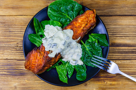Plate with roasted salmon steak, tartar sauce and spinach leaves on wooden table. Top viewの写真素材