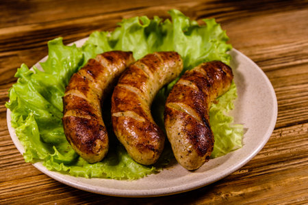 Plate with roasted sausages and lettuce leaves on wooden tableの写真素材
