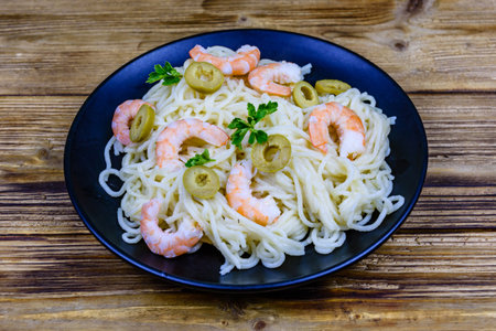 Italian pasta with shrimps and olives in black plateの写真素材