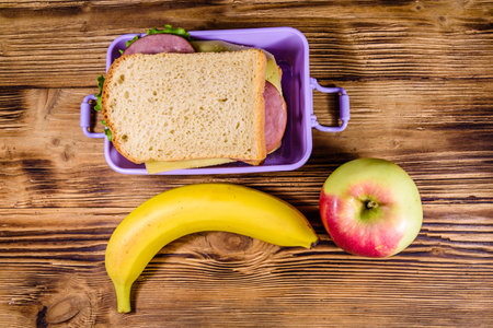 Ripe apple, banana and lunch box with sandwiches on wooden table. Top viewの写真素材