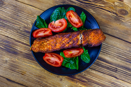 Plate with roasted salmon steak, tomatoes and spinach leaves on wooden table. Top viewの写真素材