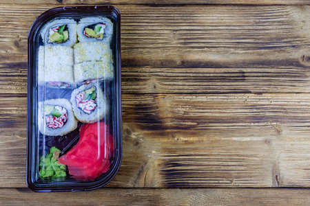 Sushi rolls in plastic box on wooden table. Top view with copy space