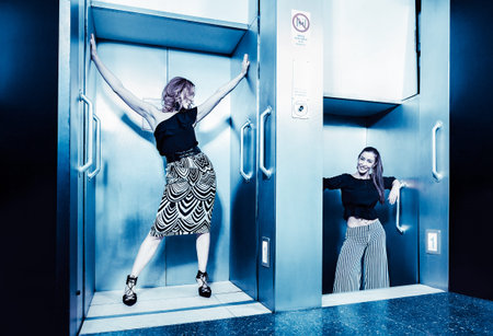 Dark color toned picture of two fashionable sexy girl in the elevator.