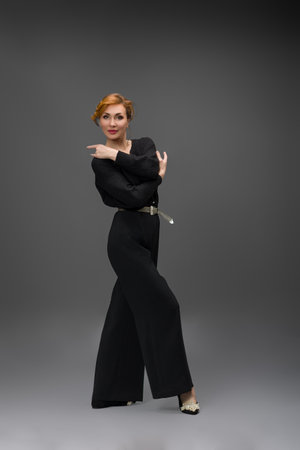 Fashion portrait of elegant woman wearing black wide leg pants and blouse with belt, standing in studio against gray background. Modern style and confident feminine look.の写真素材