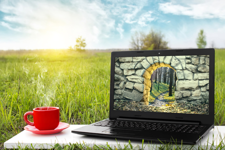 Mysterious entrance to new life or beginning. Step to new opportunities. The entrance to another world. Journey to fairytale. Laptop and a cup of hot coffee outdoors. Travel concept. Beautiful nature.の写真素材