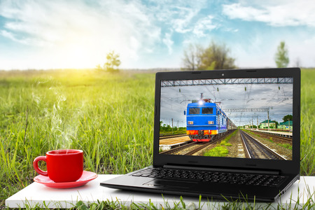 Laptop and cup of hot coffee on the background picturesque nature, outdoor office. Traveling by train. Travel concept. Business ideas. Choice of travel. Landscape at sunsetのeditorial素材