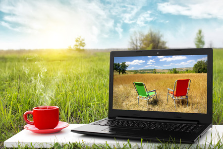 Laptop and cup of hot coffee on the background picturesque nature, outdoor office. Travel concept. Business ideas. Choice of travel. The rest of nature. Beautiful landscape.の写真素材