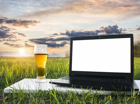Laptop on the grass and glass of cold beer at sunset. Freelance idea. Vacation concept. Beer advertising. Online store. Shop beer. Internet business. Remote work.の写真素材