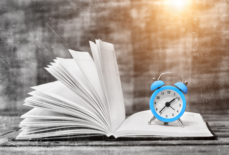 Time to read. Book and vintage alarm clock on the wooden table. Magic composition. Education concept. Prepare for the exam.の写真素材