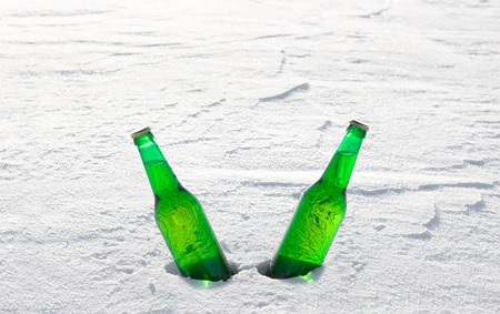 Two bottles of cold beer on the snow at sunset. Close up view.の写真素材